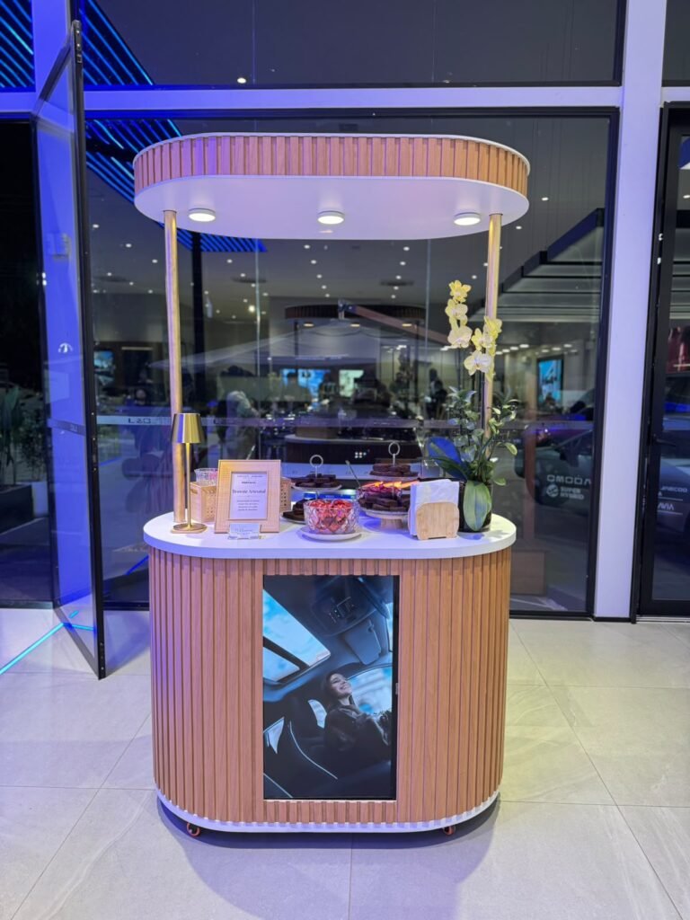 Carrinho gourmet com tela de TV exibindo vídeo, em evento corporativo
