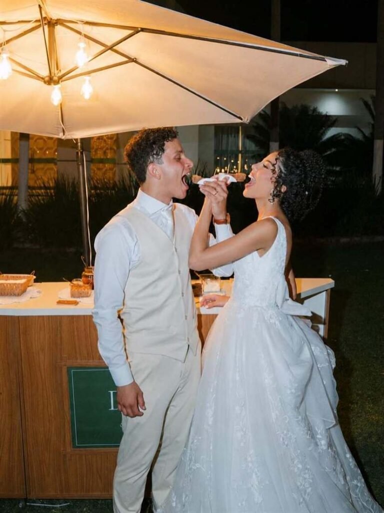 Noivos comendo churros no carrinho gourmet durante casamento à noite