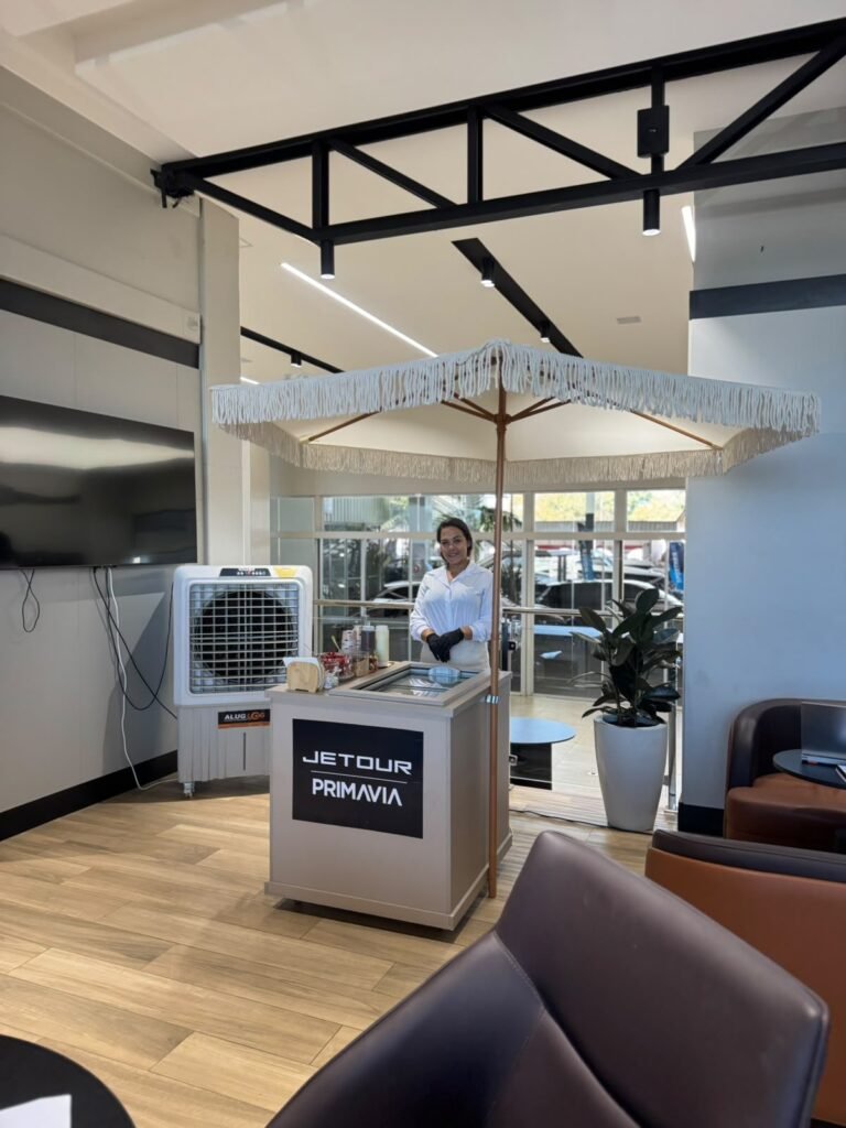Atendente no carrinho gourmet com guarda-sol franjado em evento Jetour Primavia